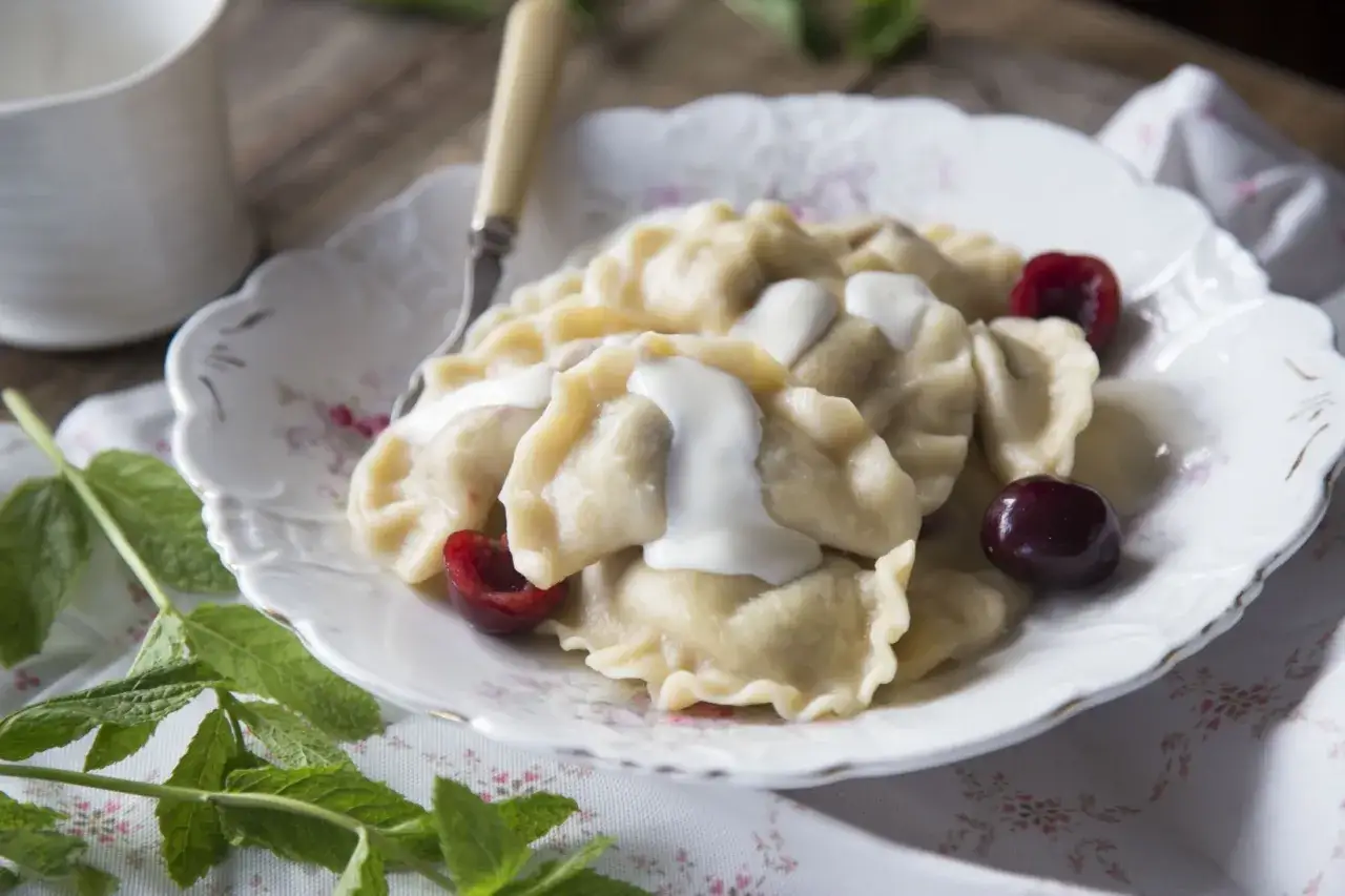 Pyszne pierogi z wiśniami, polane śmietaną, ozdobione świeżymi wiśniami i miętą. Idealne na letni deser.