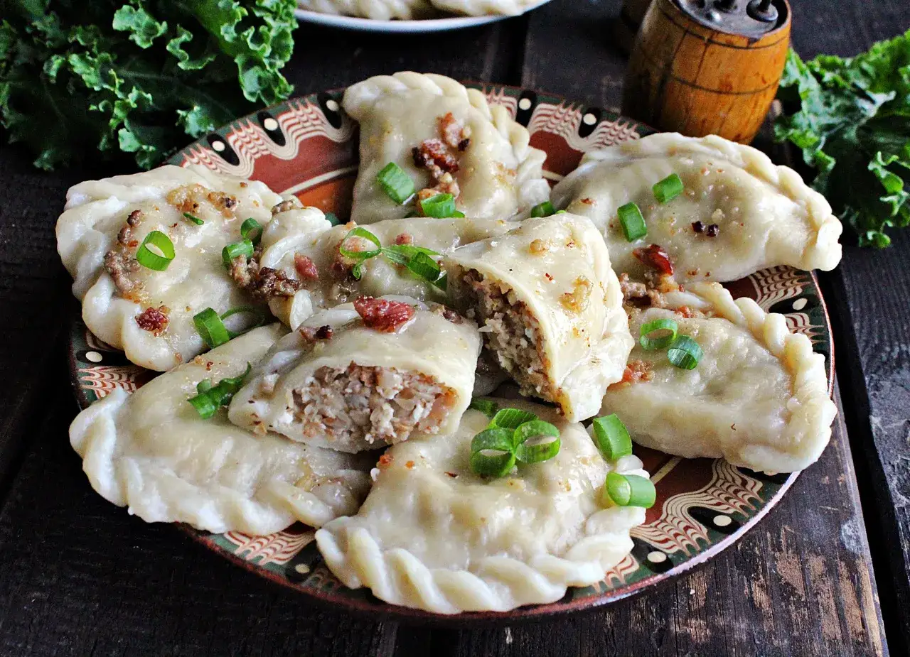 Pyszne pierogi z kaszą gryczaną, okraszone skwarkami i szczypiorkiem, kuszą na ozdobnym talerzu.