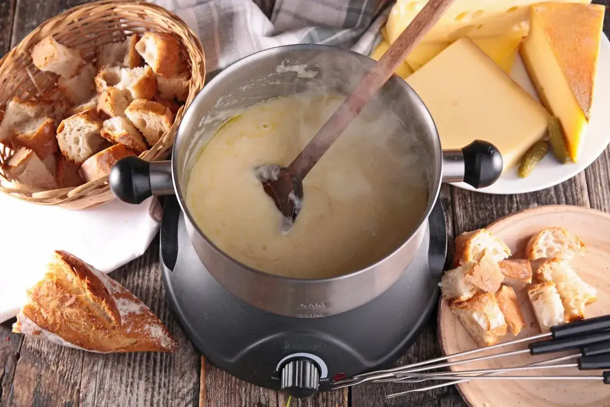 Gorące fondue serowe w garnku, obok koszyk z pieczywem i kawałki sera. Idealne na zimowe wieczory.