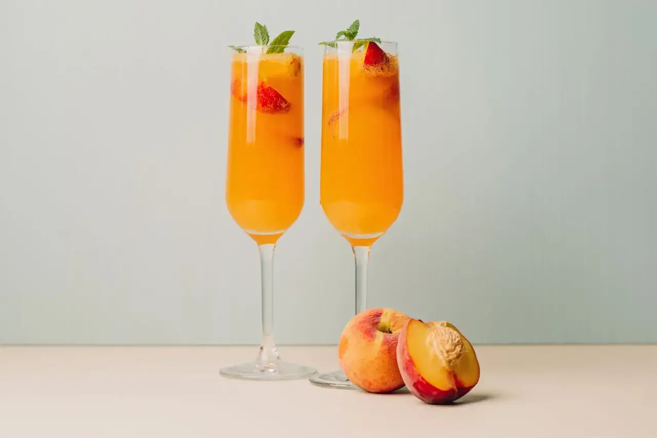 Dwa kieliszki orzeźwiającego prosecco bellini z brzoskwiniami i miętą. Obok leżą świeże brzoskwinie.