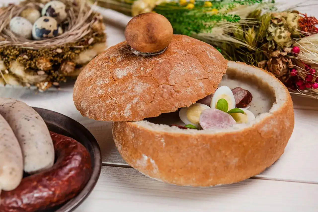 Stare przepisy na obiad: żurek w chlebie z kiełbasą i jajkiem, obok biała kiełbasa i jajka przepiórcze w gnieździe.