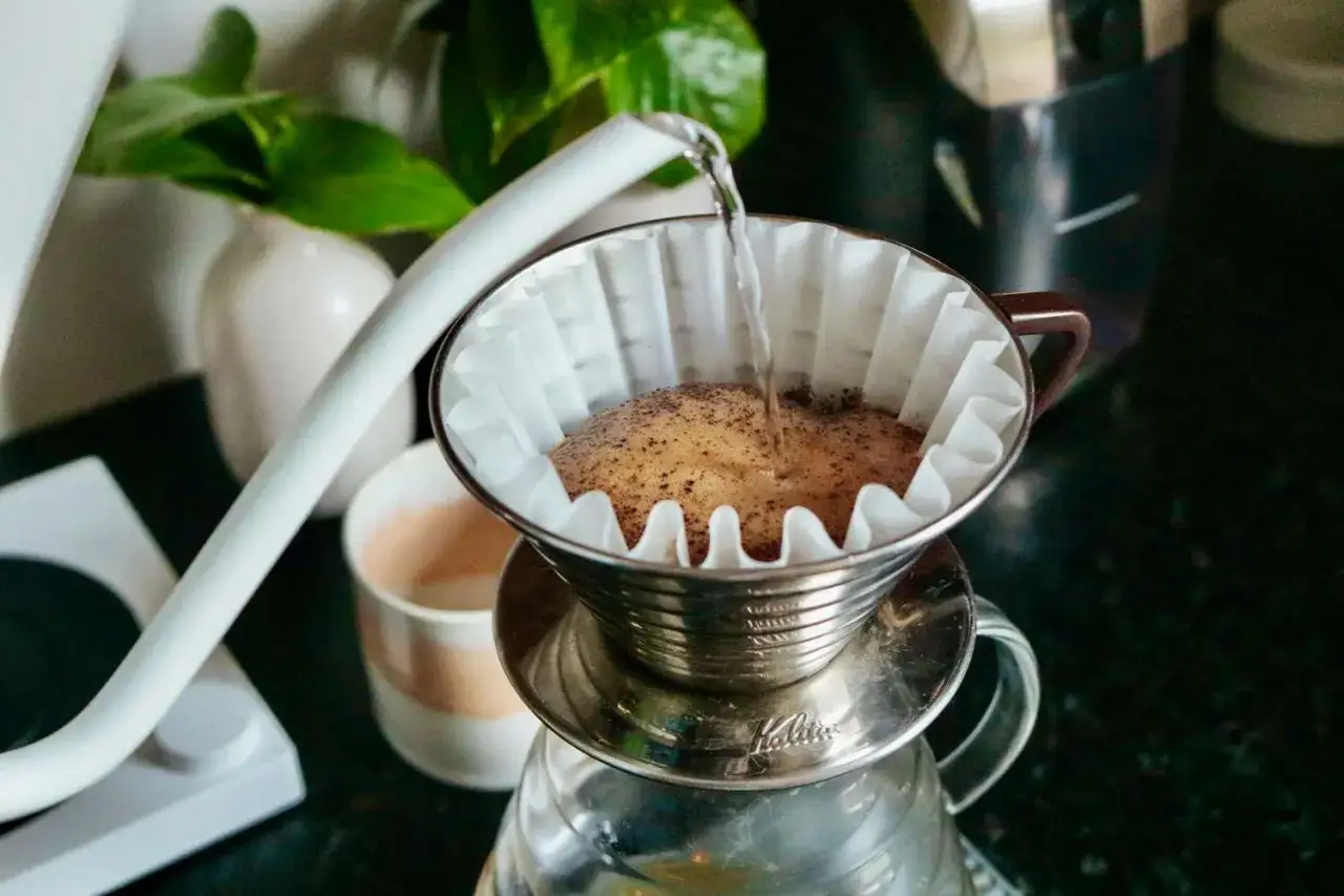 Parzenie kawy metodą przelewową. Gorąca woda spływa na mielone ziarna, tworząc aromatyczny napój, idealny na pobudzenie jak red eye coffee.