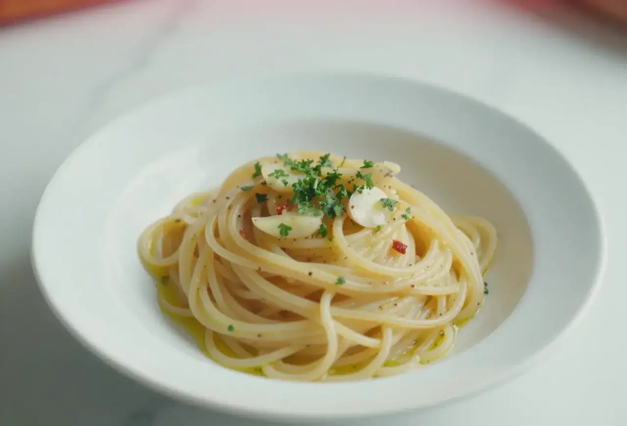 Pyszny makaron aglio olio z czosnkiem, natką pietruszki i płatkami chili na białym talerzu.