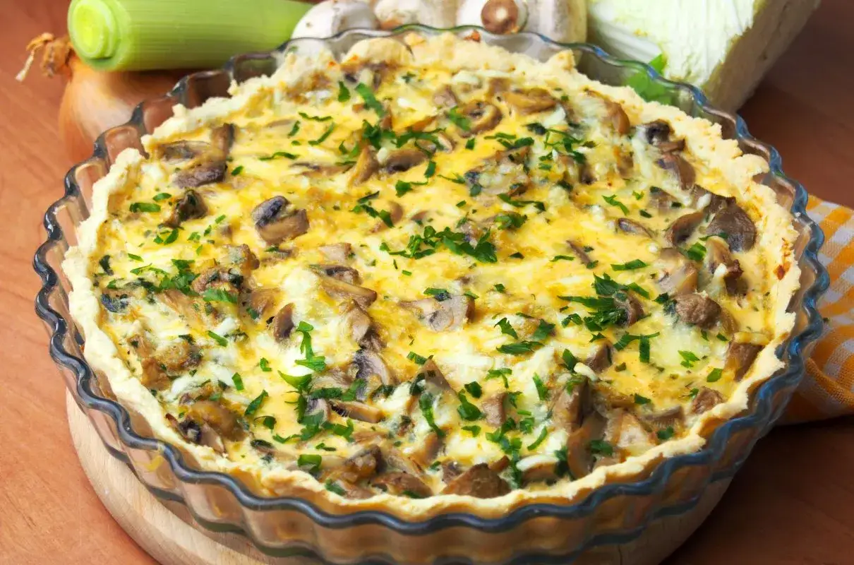 Pyszna tarta z pieczarkami i porem, posypana świeżą natką pietruszki, w szklanej formie.