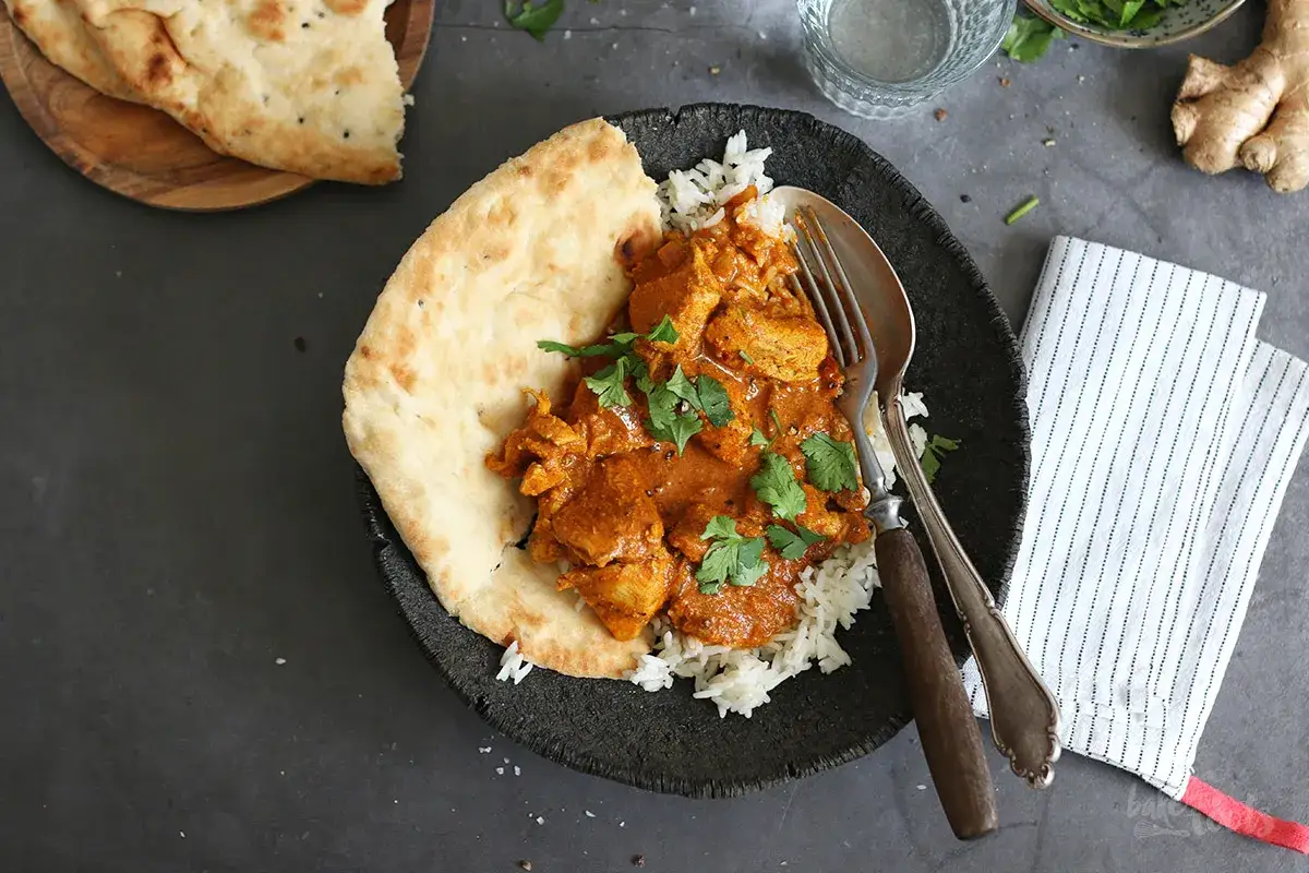 Pyszny kurczak butter chicken z ryżem i chlebkiem naan, udekorowany świeżą kolendrą.
