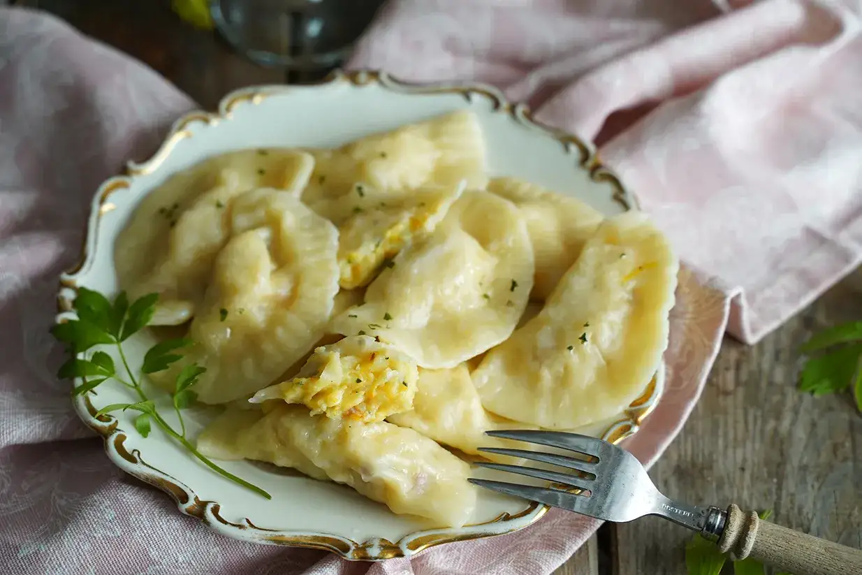 Pyszne pierogi z dynią, delikatnie posypane natką pietruszki, czekają na widelcu.