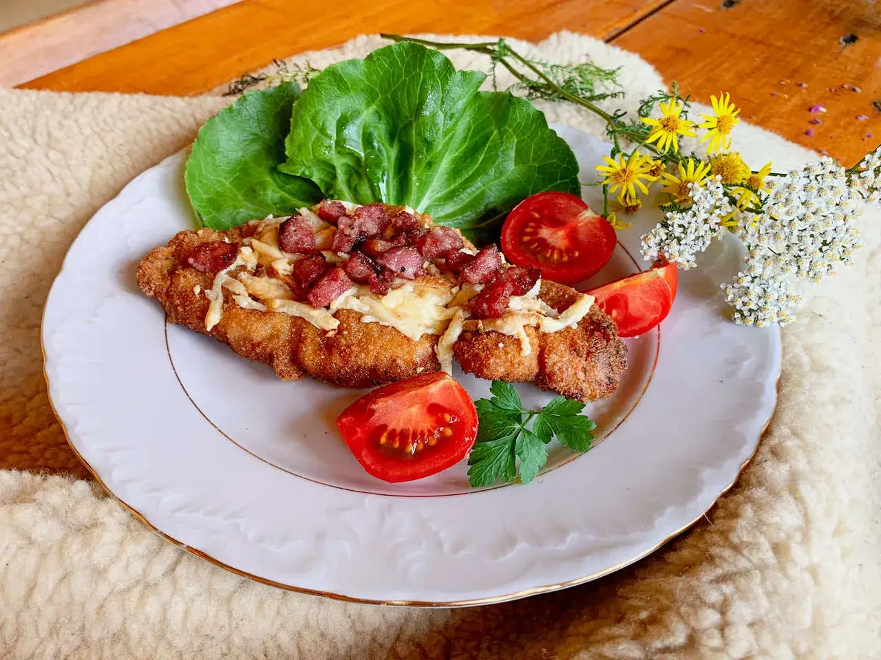 Pyszny kotlet schabowy z serem i boczkiem, udekorowany pomidorami i świeżymi ziołami.